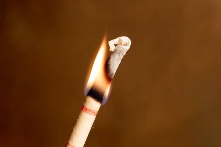 Close-up of a burning incense stick with a small flame and smoke, against a plain brown background, evoking the calming ambience often found in serene spaces like a medical center.