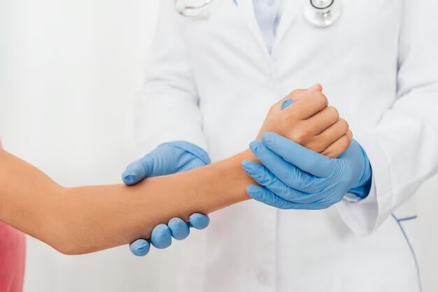 At the walk-in clinic, a person in a white coat and stethoscope checks another person's wrist while wearing blue gloves.